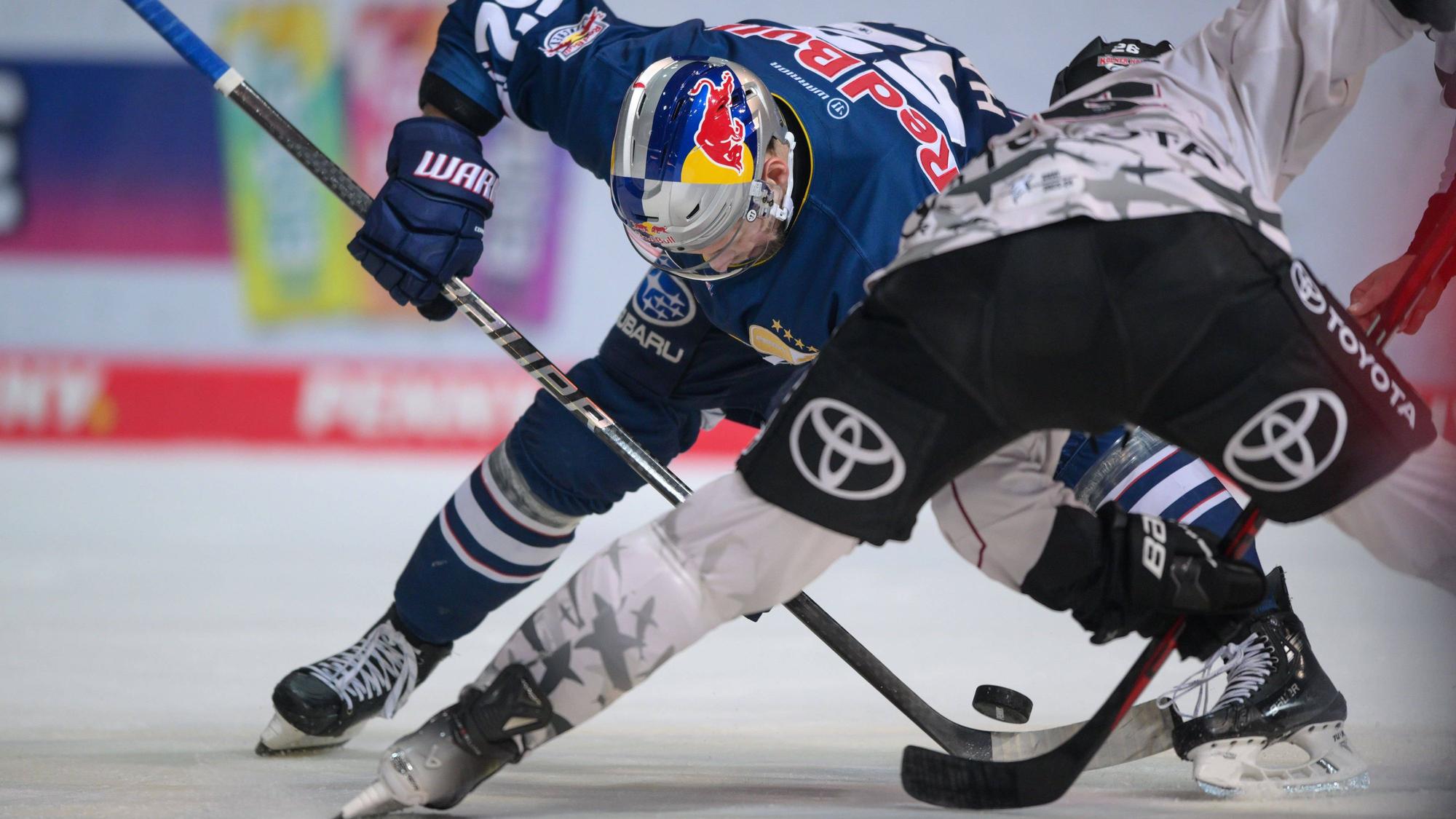 Eishockeyspieler fahren aus gegenübersetzten Richtungen auf einen Puck zu, bei dem sich ihre Schläger treffen.