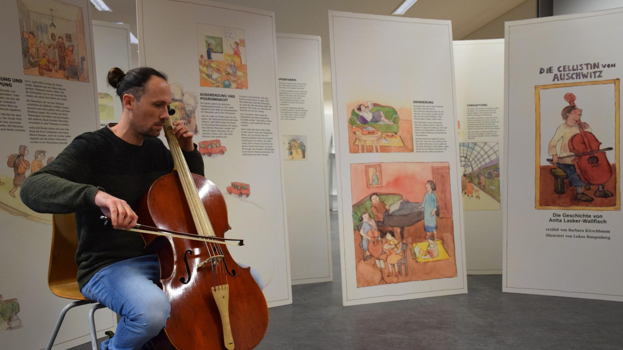 Ein Cello-Spieler sitzt vor Aufstellern.