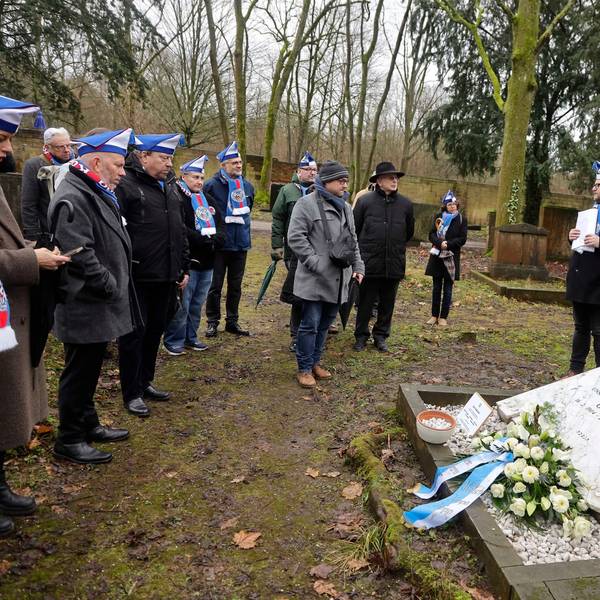 Eine Gruppe Menschen steht an einer Gedenktafel auf einem Friedhof.