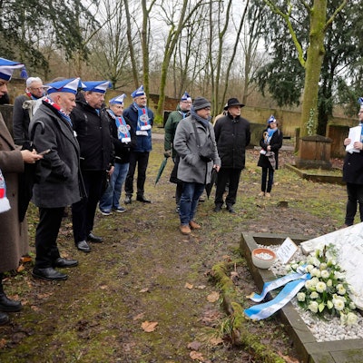 Eine Gruppe Menschen steht an einer Gedenktafel auf einem Friedhof.