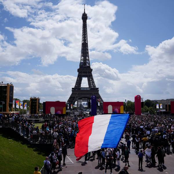 Ein Mann entrollt Fahne in den Farben der französische Nationalflagge in der olympischen Fanzone im Trocadero-Garten vor dem Eiffelturm.