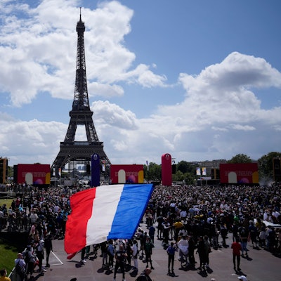 Ein Mann entrollt Fahne in den Farben der französische Nationalflagge in der olympischen Fanzone im Trocadero-Garten vor dem Eiffelturm.