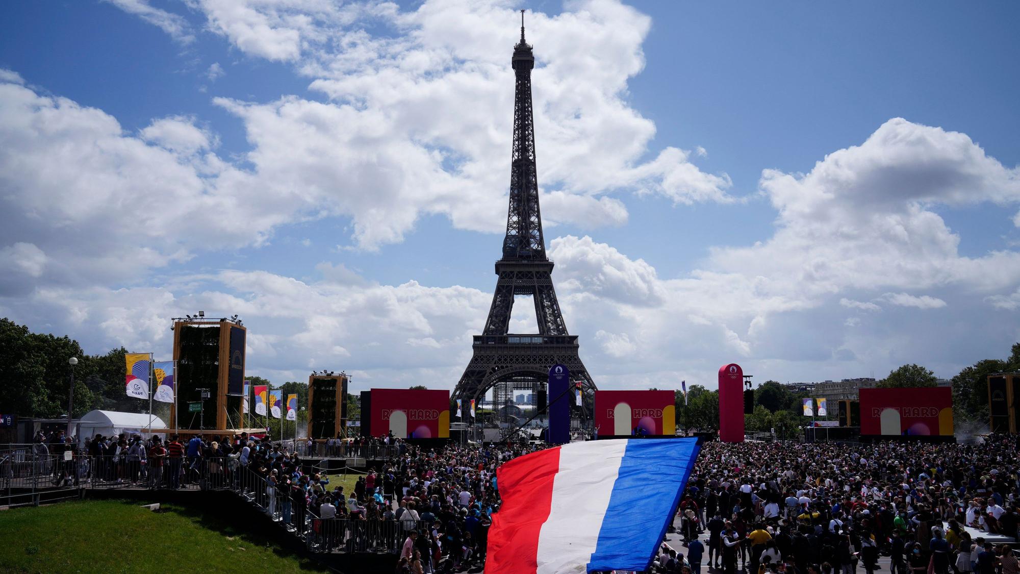 Ein Mann entrollt Fahne in den Farben der französische Nationalflagge in der olympischen Fanzone im Trocadero-Garten vor dem Eiffelturm.