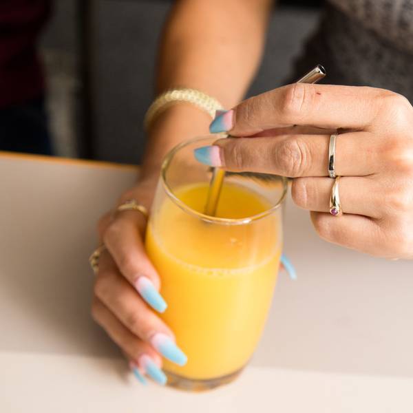Eine Frau mit bunten Fingernägeln trinkt mit einem Strohhalm aus einem Glas Orangensaft.