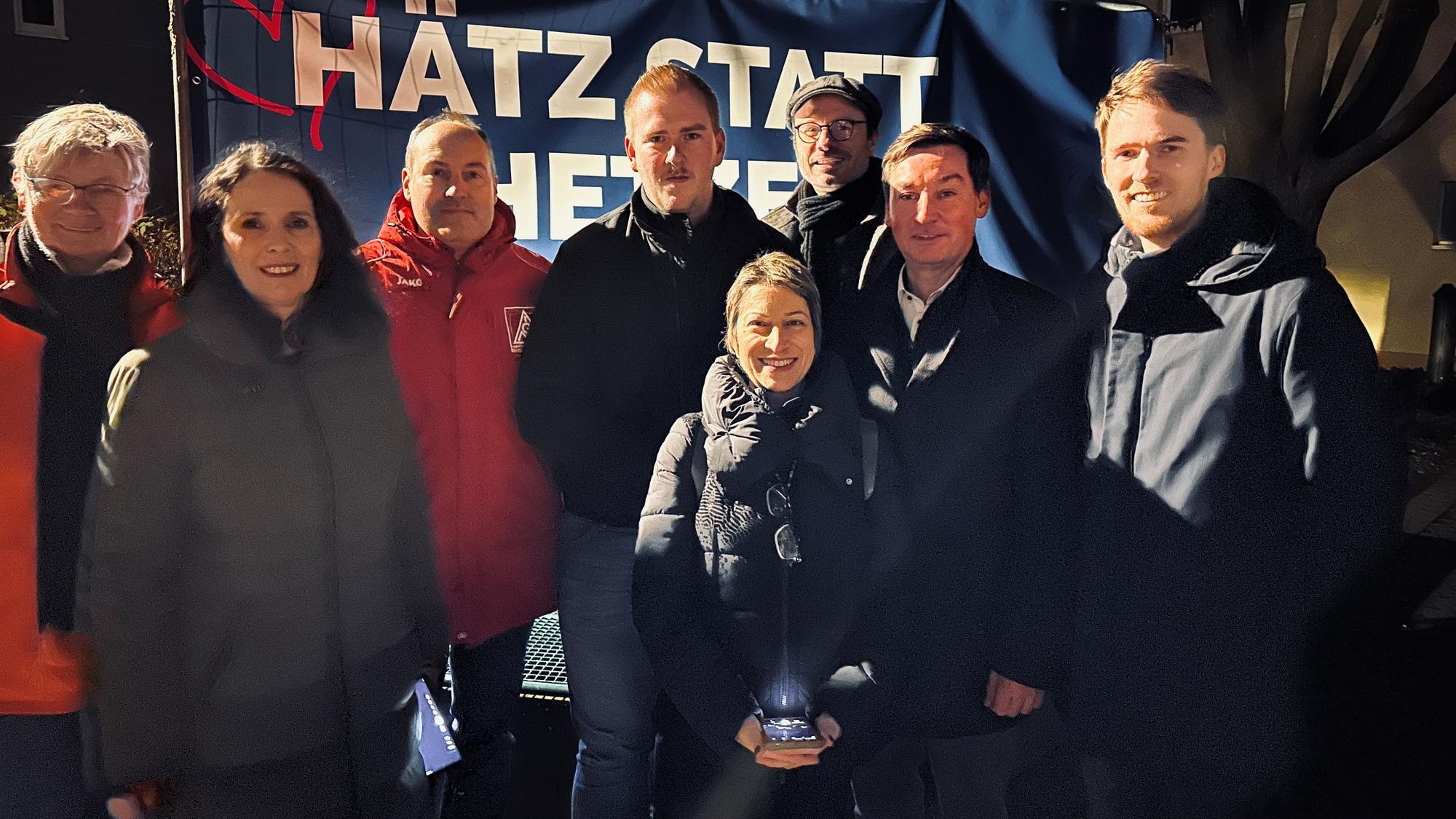 Männer und Frauen stehen vor einem Banner mit der Aufschrift „Hätz statt Hetze“.