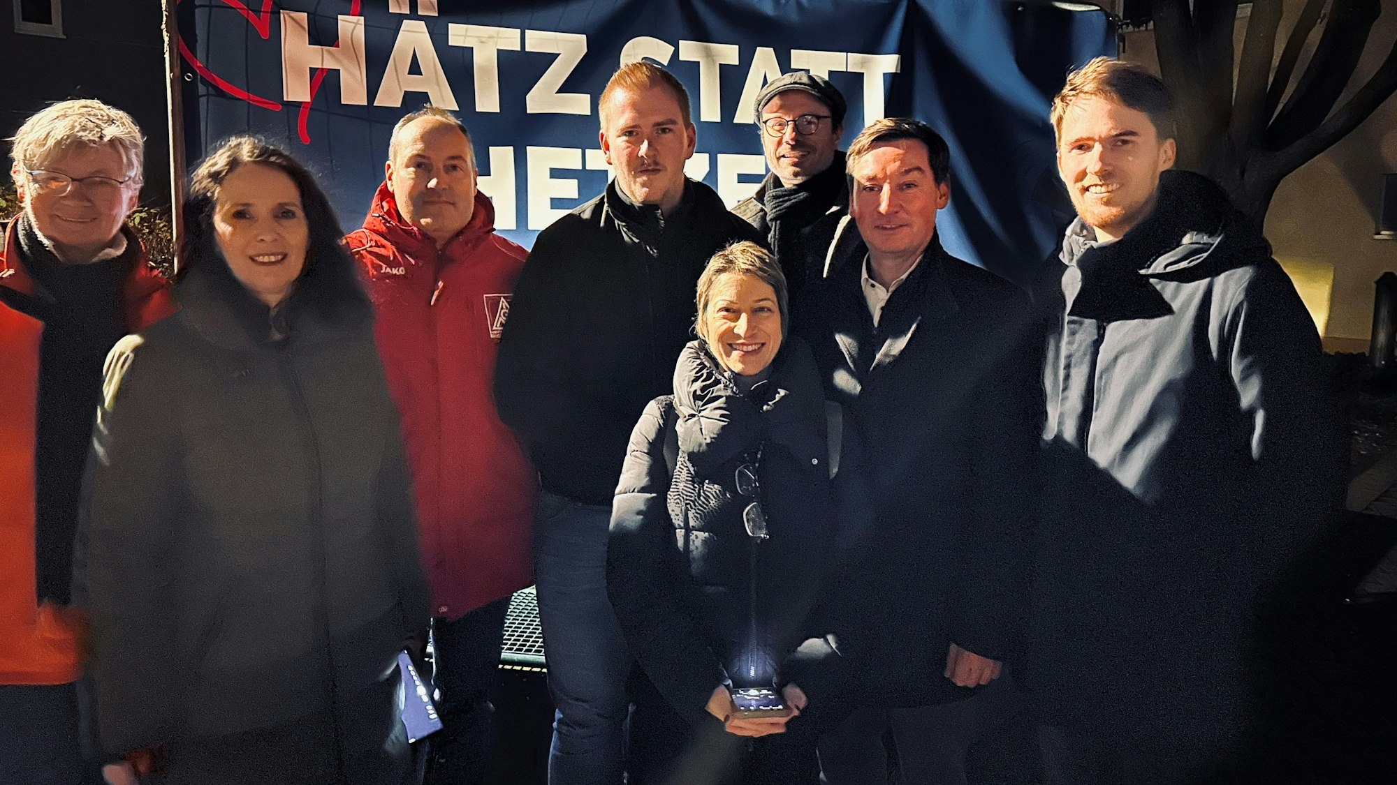 Männer und Frauen stehen vor einem Banner mit der Aufschrift „Hätz statt Hetze“.