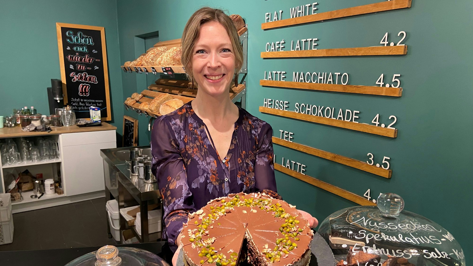 Auf dem Bild ist eine Frau in ihrem Café zu sehen, sie hält eine Schokotorte in die Kamera.
