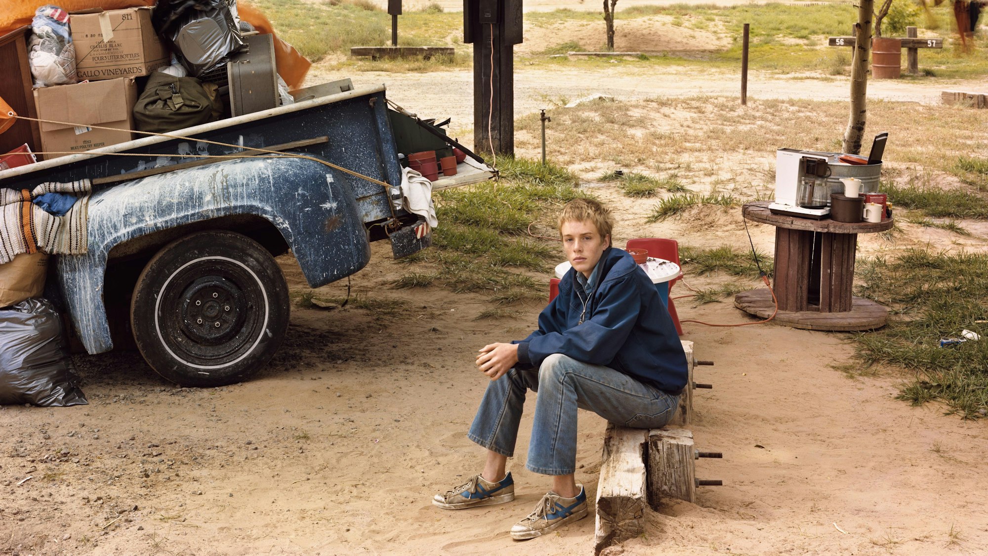 Ein Junge sitzt auf einem Campingplatz neben einem vollgepackten Lastwagen.