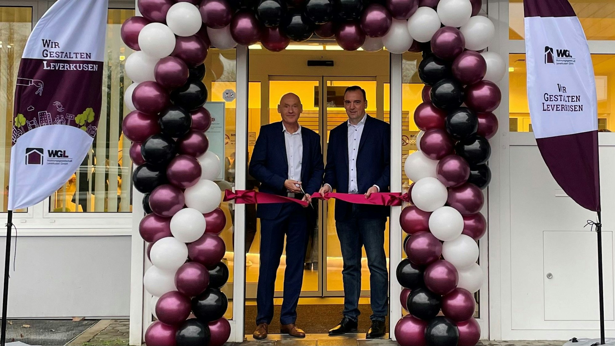 Geschäftsführer Gerald Hochkamer und Abteilungsleiter Thomas Seidel durchschneiden zur Eröffnung ein pinkes Band vor der Eingangstür des neuen Service-Centers der Wohnungsgesellschaft Leverkusen GmbH.
