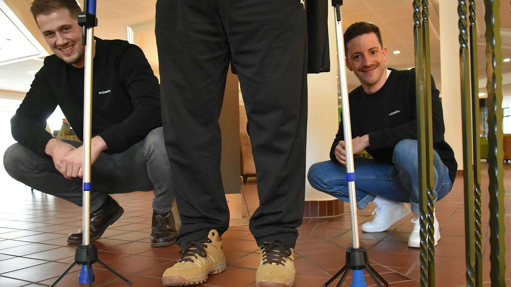 Zu sehen sind zwei junge Männer und ihre an Krücken installierten Umfallhilfen.