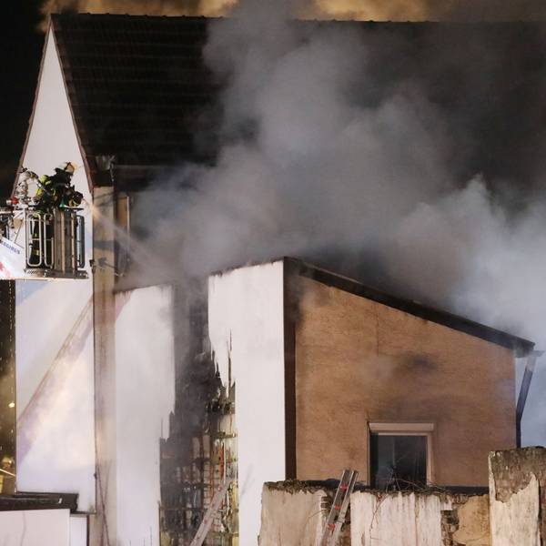 Feuerwehrleute löschen von einer Drehleiter aus ein brennendes Gebäude. Es dringt dichter Rauch aus dem Haus