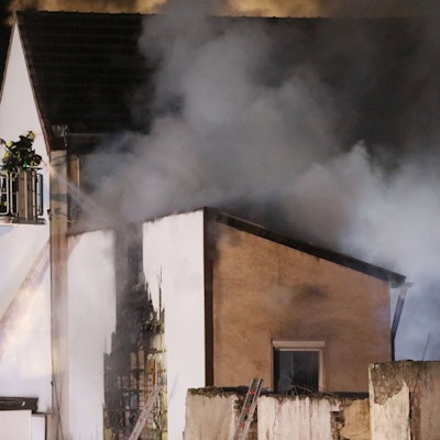 Feuerwehrleute löschen von einer Drehleiter aus ein brennendes Gebäude. Es dringt dichter Rauch aus dem Haus