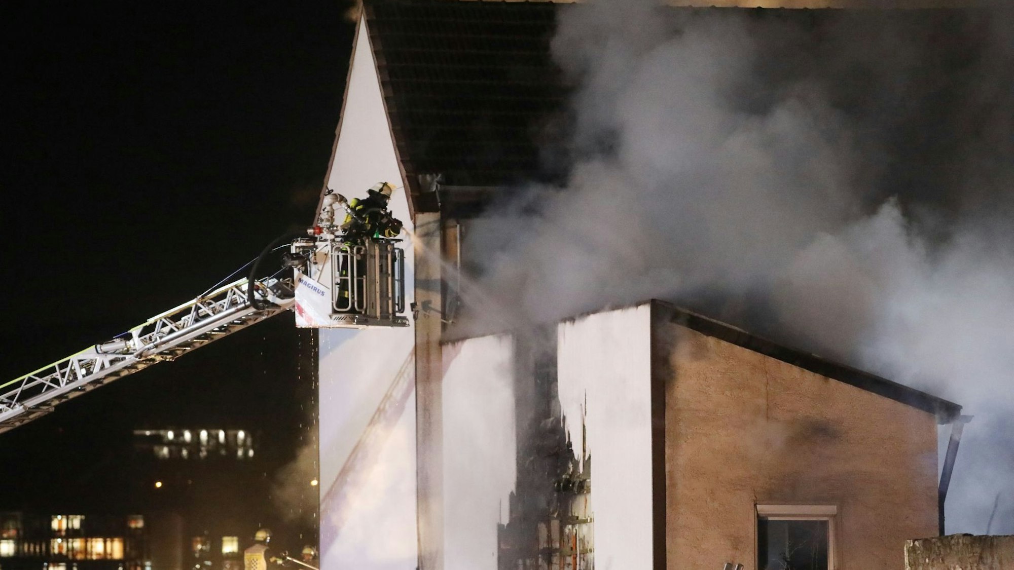 Feuerwehrleute löschen von einer Drehleiter aus ein brennendes Gebäude. Es dringt dichter Rauch aus dem Haus