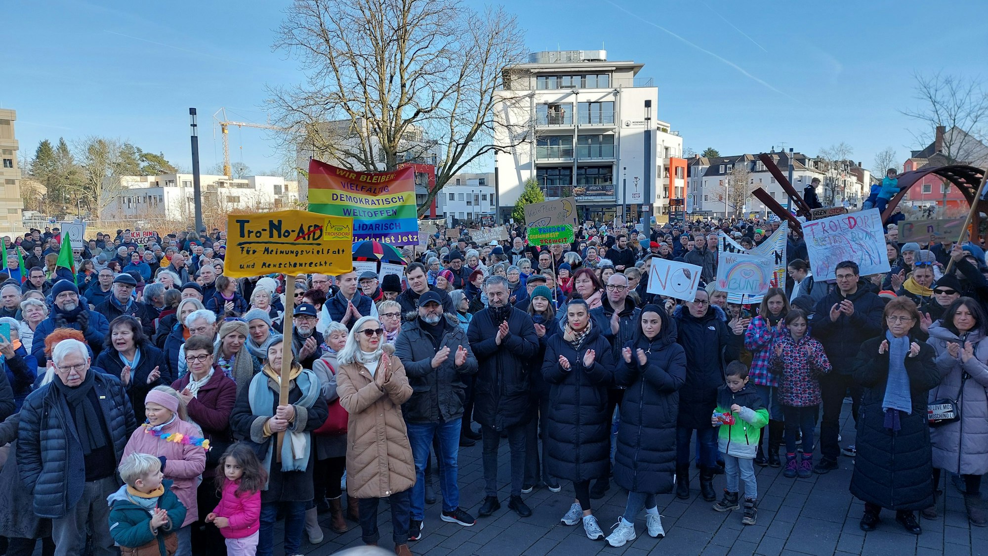 Eine große Menschenmenge steht auf einem Platz. Erwachsene und Kinder tragen Protestschilder.