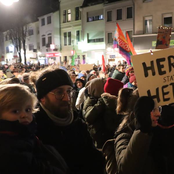 Tausende Menschen stehen zusammen und halten Plakate und Fahnen hoch.