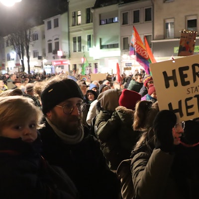 Tausende Menschen stehen zusammen und halten Plakate und Fahnen hoch.