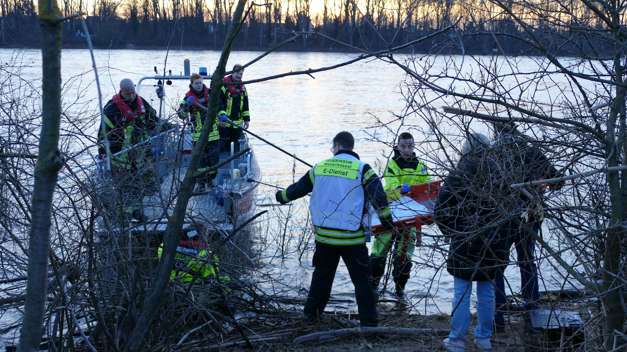 Feuerwehrleute und Angehörige der Kriminalpolizei stehen im Ufergestrüpp.