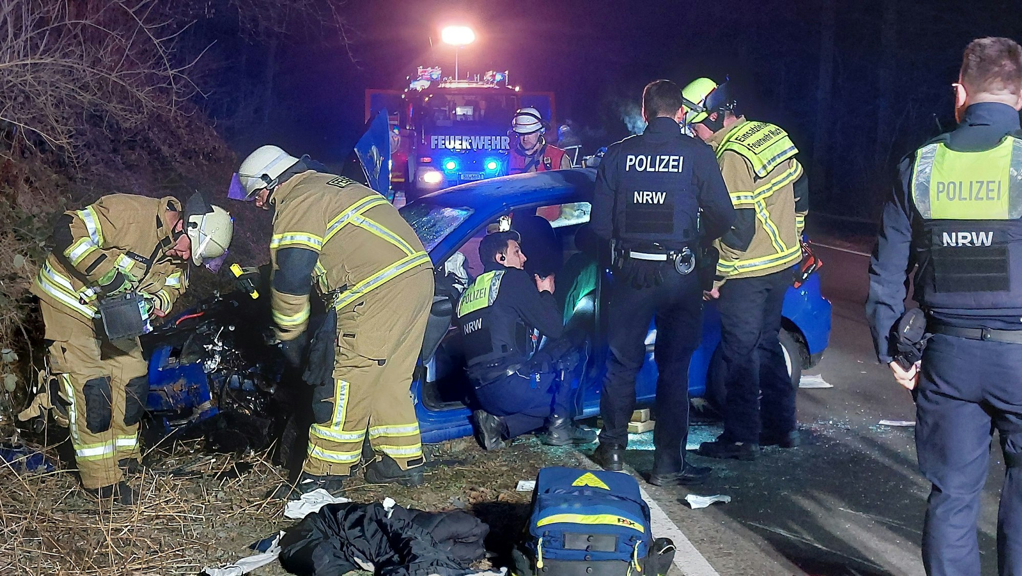 Feuerwehrleute und Polizisten stehen um das Autowrack herum.