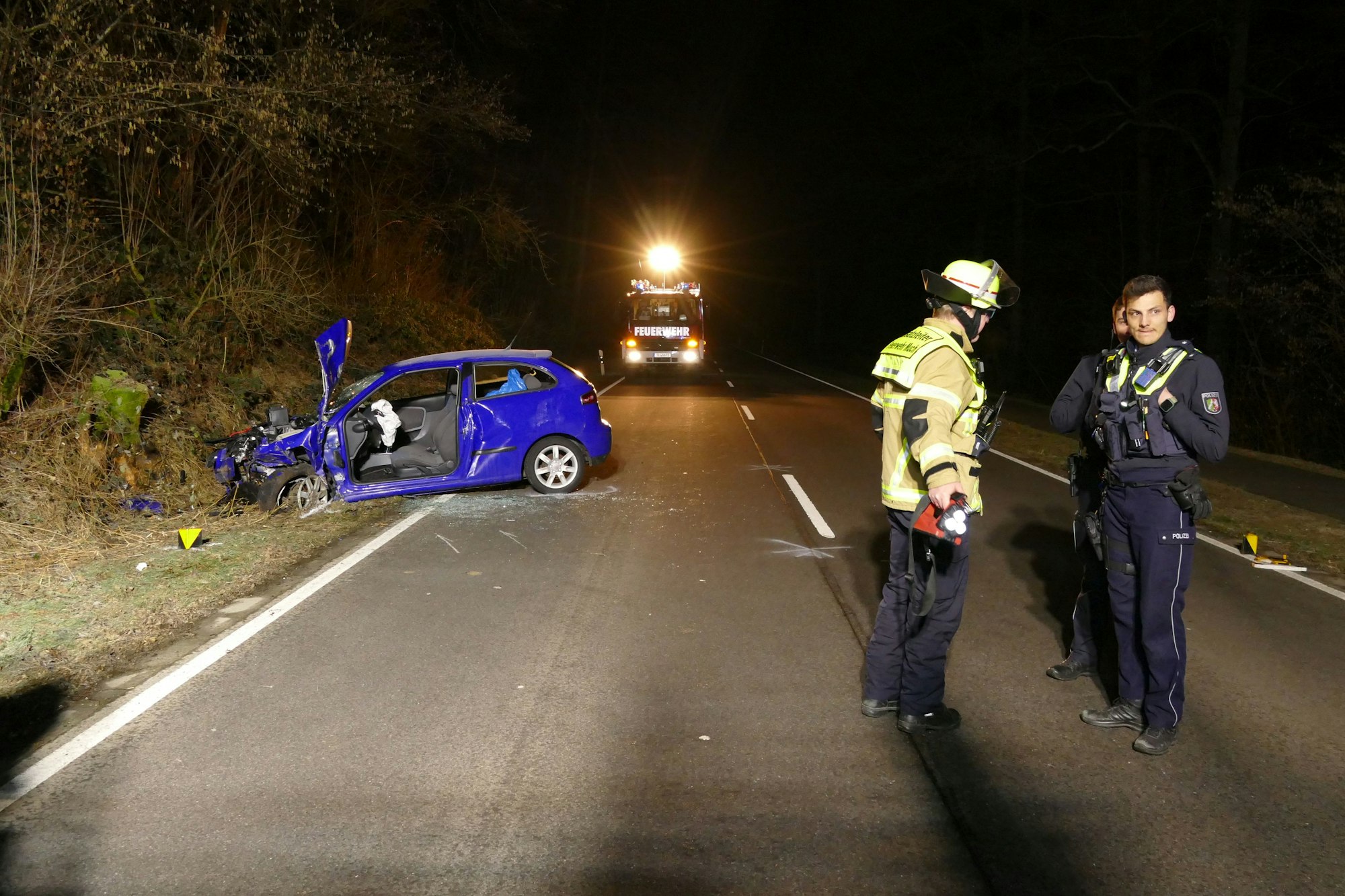 Ein Auto liegt im Straßengraben, Polizisten und ein Feuerwehrmann stehen umher.