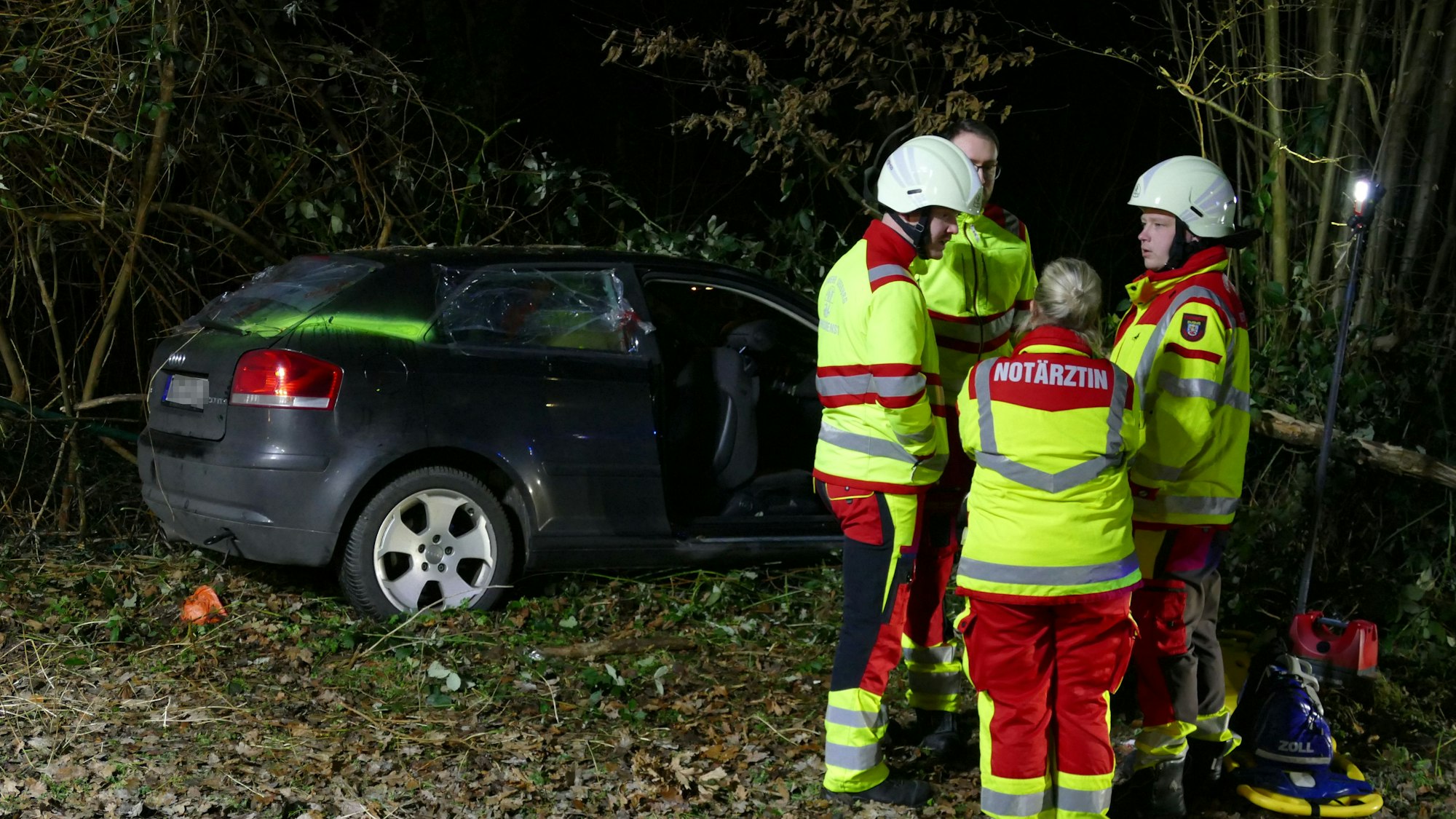 Rettungskräfte stehen um das verunglückte Auto herum.