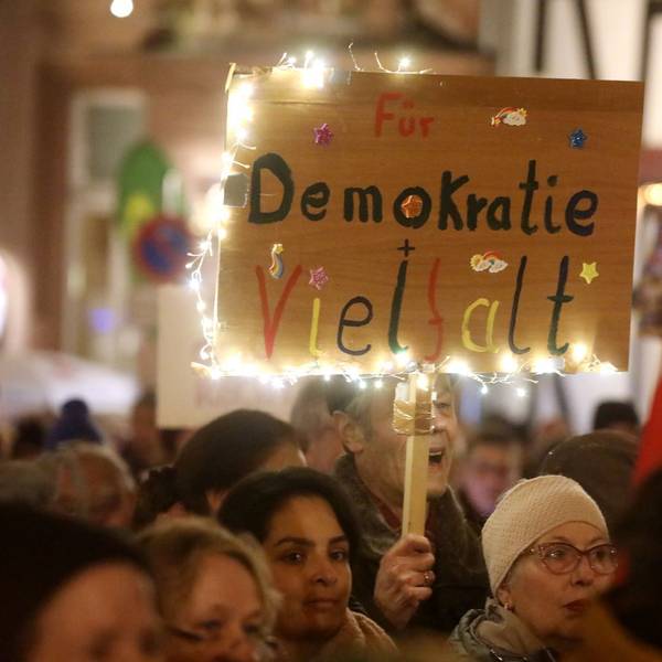 Teilnehmer einer Kundgebung halten Fahnen und Protestschilder. „Für Demokratie und Vielfalt“ steht auf einem bunten Schild mit Lichterkette.