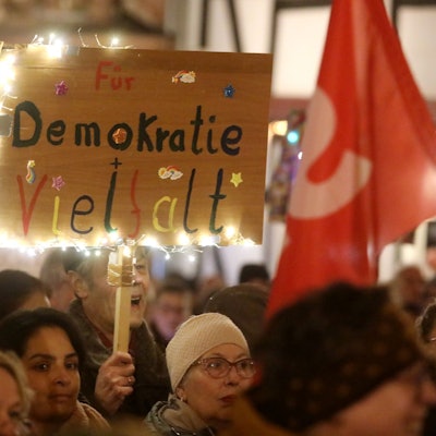 Teilnehmer einer Kundgebung halten Fahnen und Protestschilder. „Für Demokratie und Vielfalt“ steht auf einem bunten Schild mit Lichterkette.