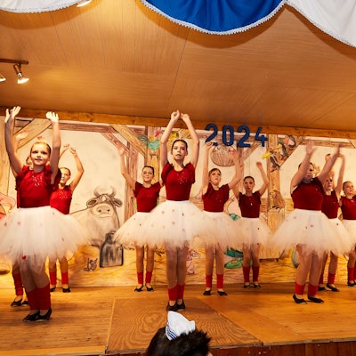 Eine Gruppe junger Mädchen tanzt in weißen Tüll-Röcken und roten T-Shirts auf einer Bühne.