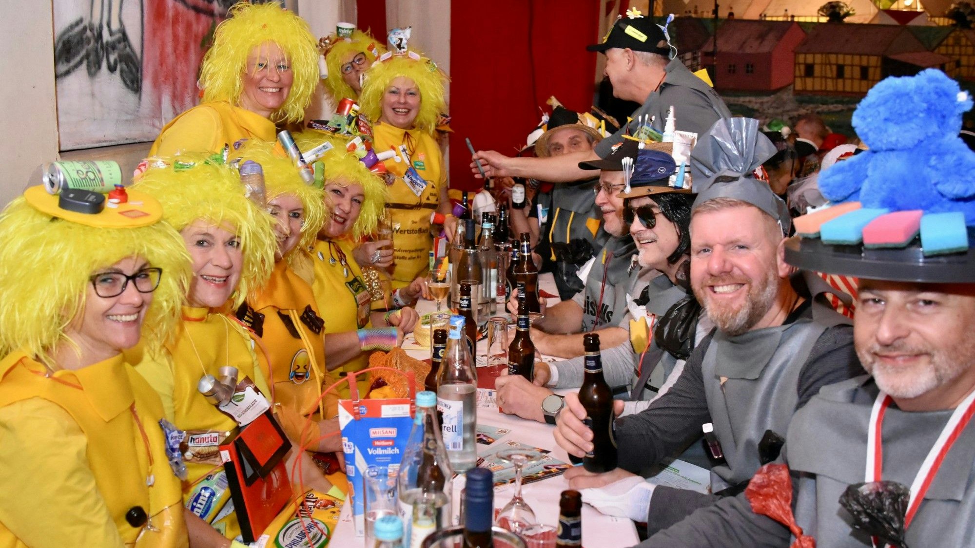 Besucher einer Karnevalssitzung: Links sitzen Frauen in gelben Kostümen, die Wertstoffbeutel darstellen, rechts Männer in grauen Kostümen als Beistellsack zur Restmülltonne.