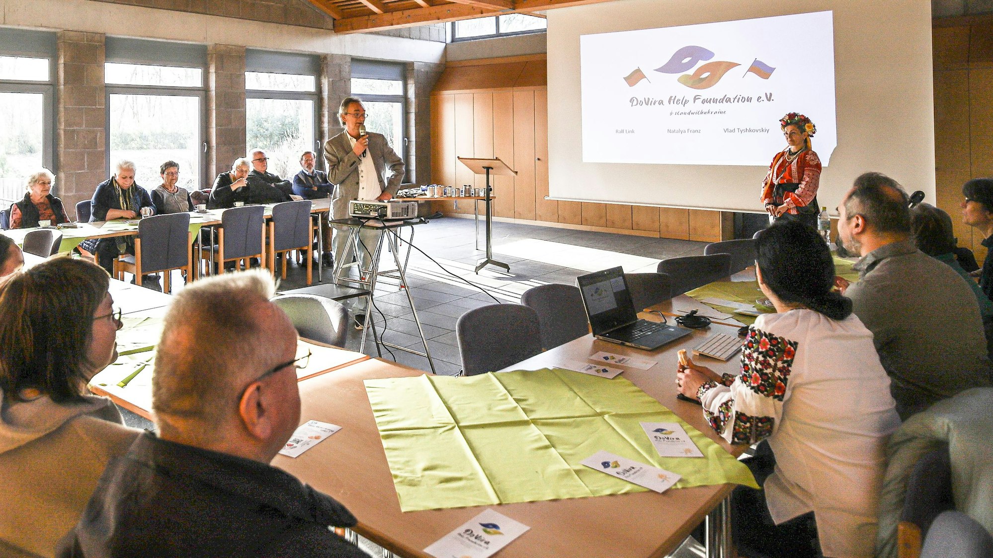 Männer und Frauen sitzen um eine Tisch bei einem Vortrag.