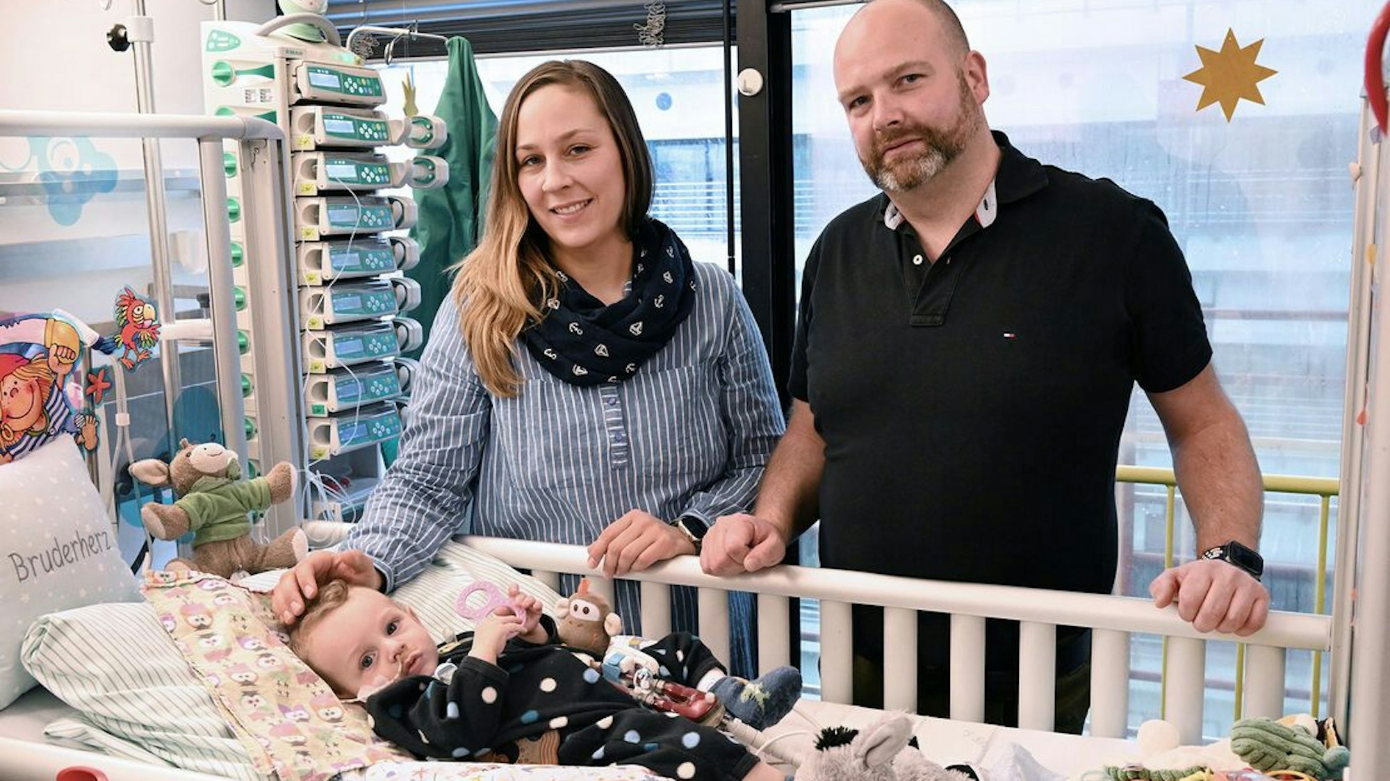 Ein Mann und eine Frau stehen am Krankenbett eines Säuglings.