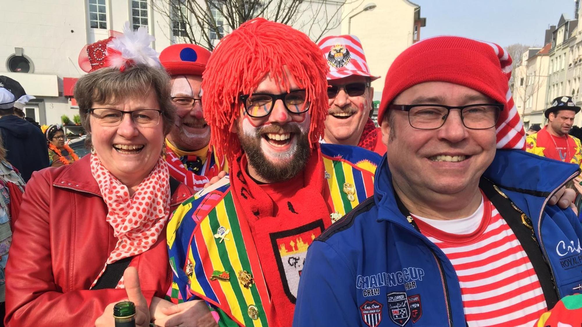 Kostümierte Menschen strahlen in die Kamera, sie stehen auf einem Platz bei strahlendem Sonnenschein.