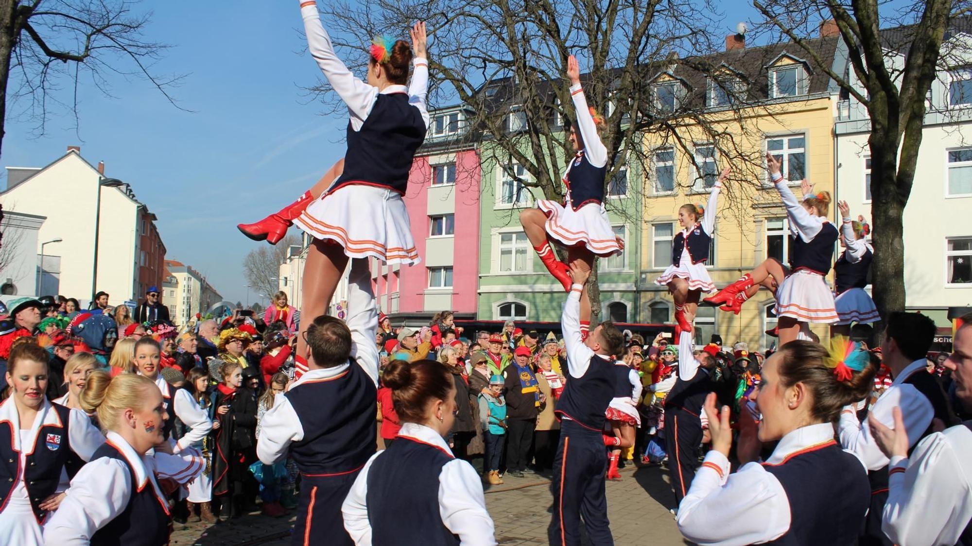 Bunt kostümierte Menschen stehen um einen Stehtisch auf einem Platz.