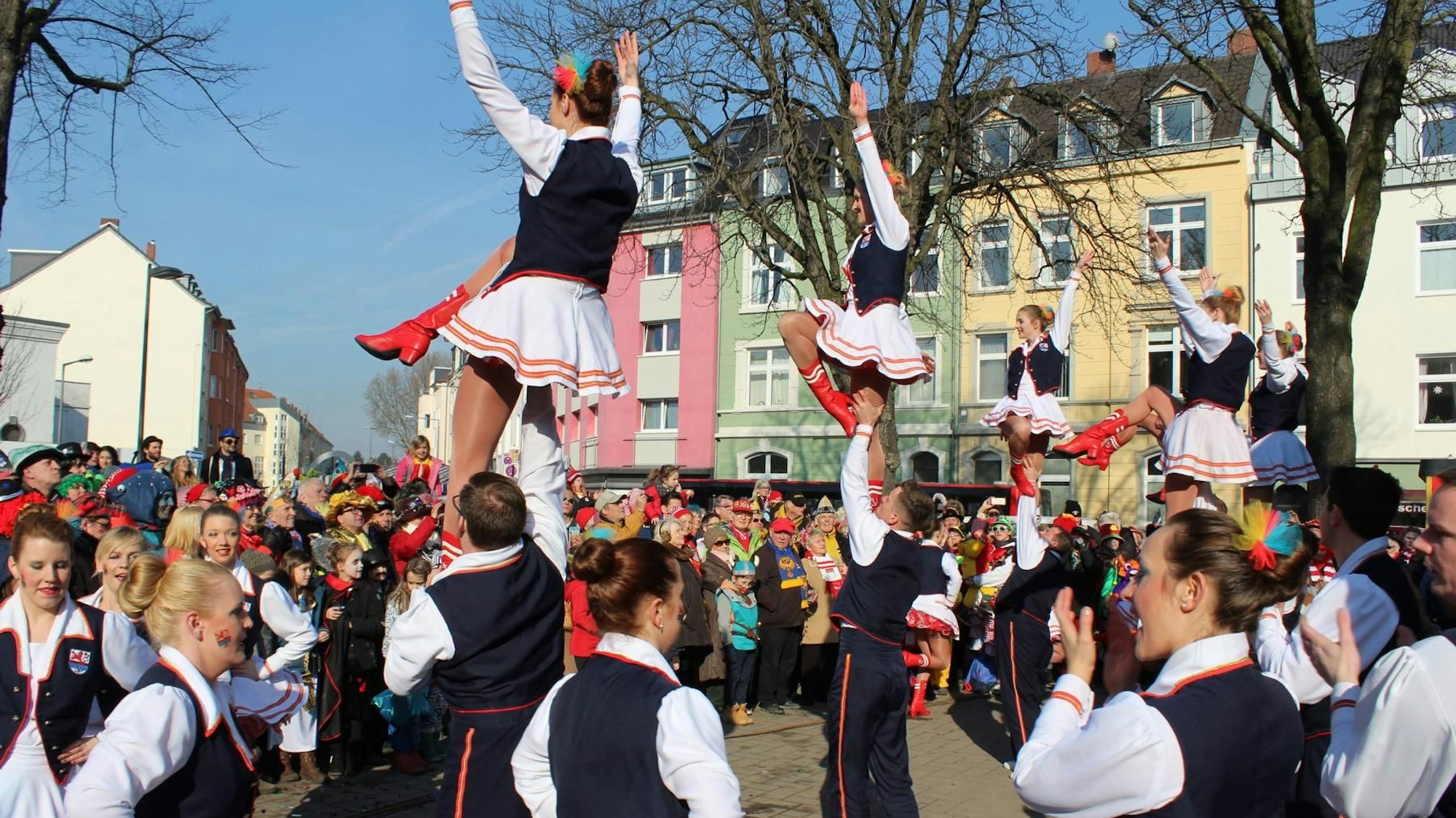 Bunt kostümierte Menschen stehen um einen Stehtisch auf einem Platz.