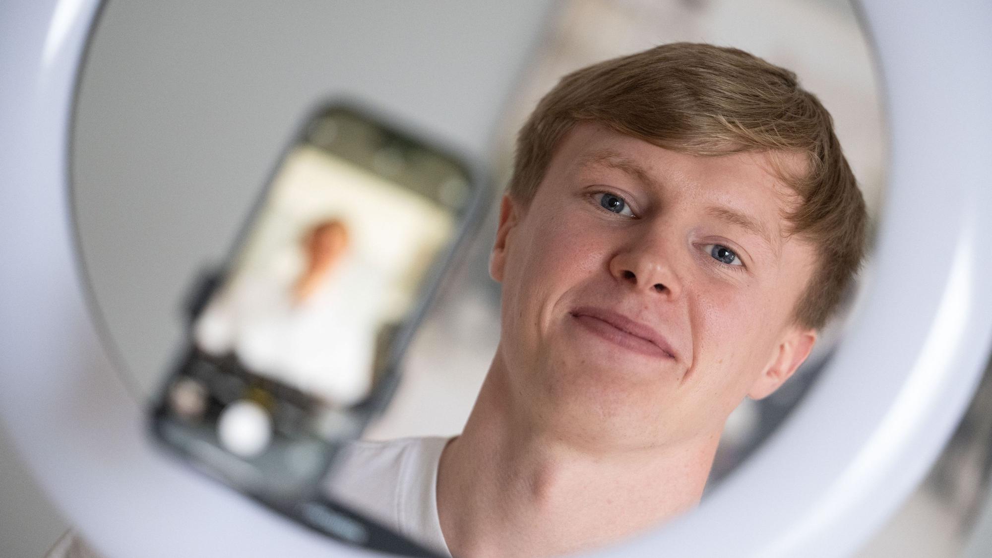 Der Influencer Liam Carpenter steht in seiner Wohnung hinter einem Stativ, auf dem ein Smartphone und ein Ringlicht montiert sind.