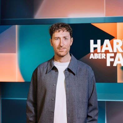 Moderator Louis Klamroth steht vor dem Logo der ARD-Talkshow „Hart aber fair“ in einem Fernsehstudio. Das Aussehen und die inhaltliche Ausrichtung des Formats ändern sich ab Januar 2024.