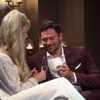 Eine Frau und ein Mann sitzen auf einem Sofa und stoßen mit ihren Gläsern an.