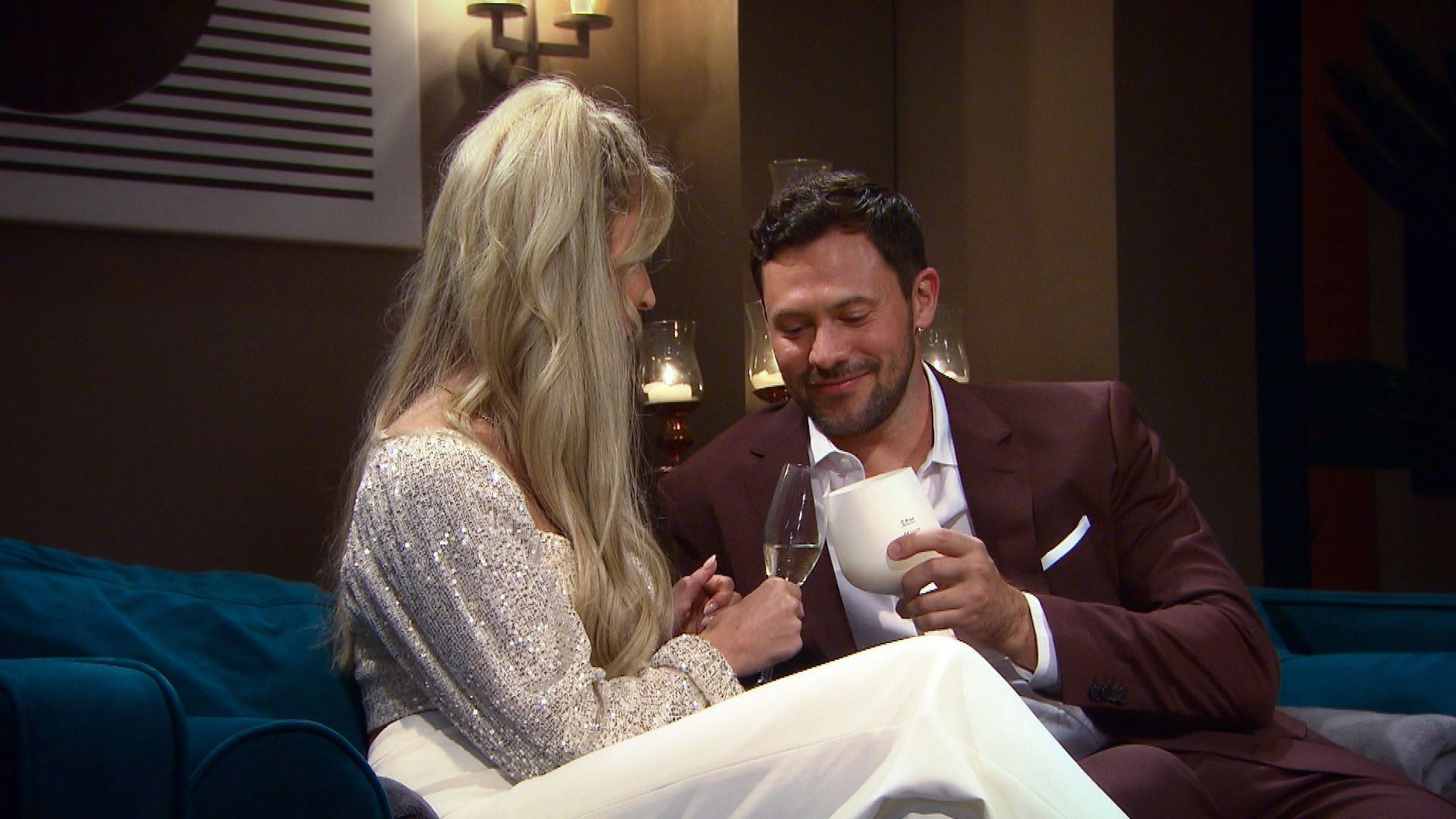 Eine Frau und ein Mann sitzen auf einem Sofa und stoßen mit ihren Gläsern an.