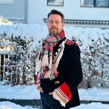 Der Zugleiter steht vor einer Hecke.