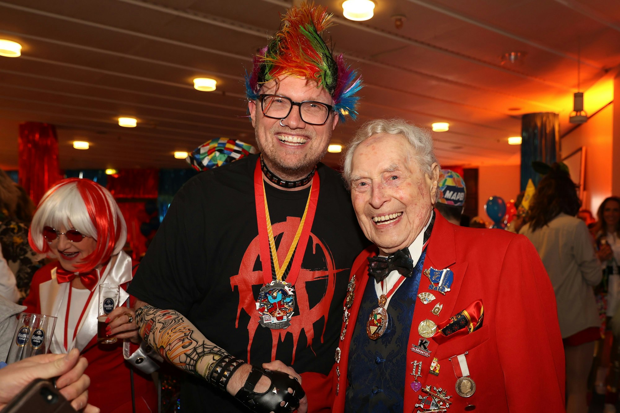 Jochen Ott mit bunter Perücke, Nasenpiercing und falschen Tattoos neben Ludwig Sebus