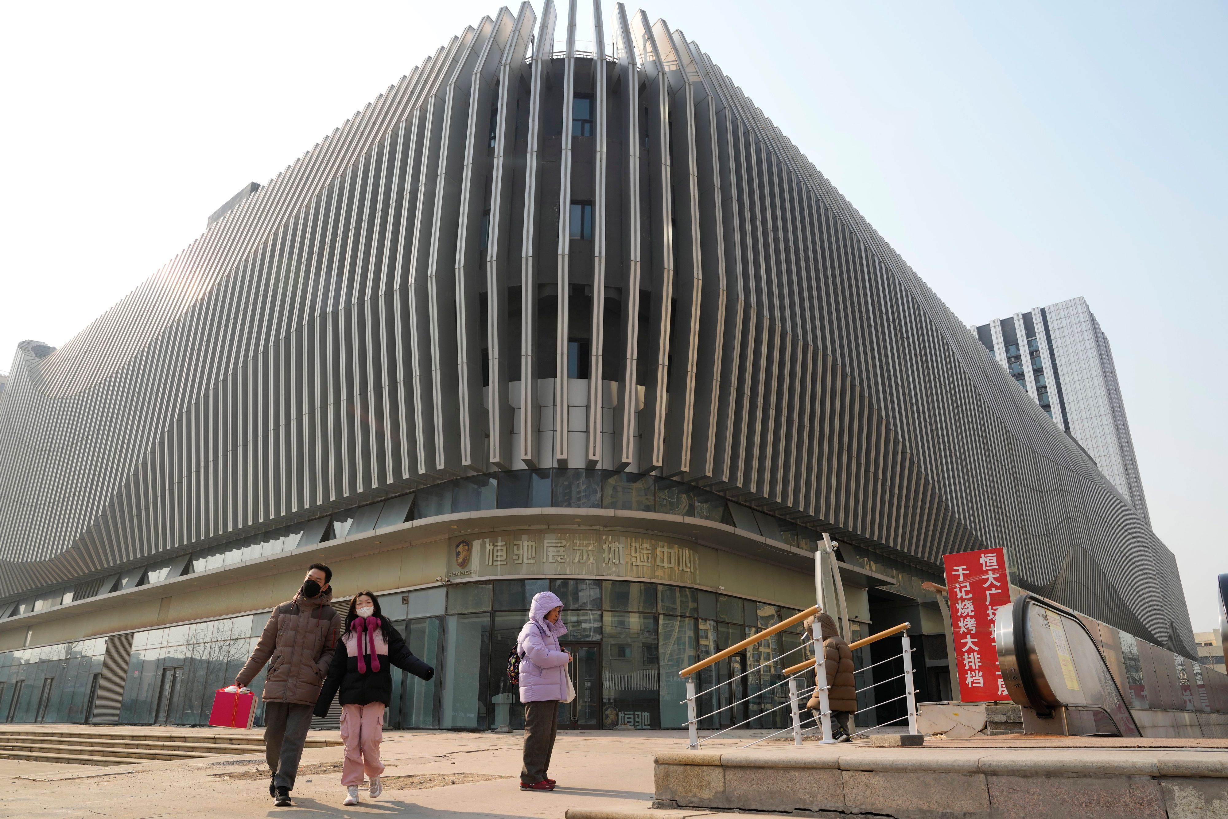 29.01.2024, China, Peking: Anwohner gehen an einem Evergrande-Geschäftskomplex mit einem verschlossenen Evergrande-Autohaus in Peking vorbei. Der chinesische Immobilienentwickler China Evergrande Group wurde am Montag von einem Gericht in Hongkong zur Liquidation verurteilt, nachdem das Unternehmen nicht in der Lage war, eine Umstrukturierungsvereinbarung mit seinen Gläubigern zu treffen. Foto: Ng Han Guan/AP/dpa +++ dpa-Bildfunk +++