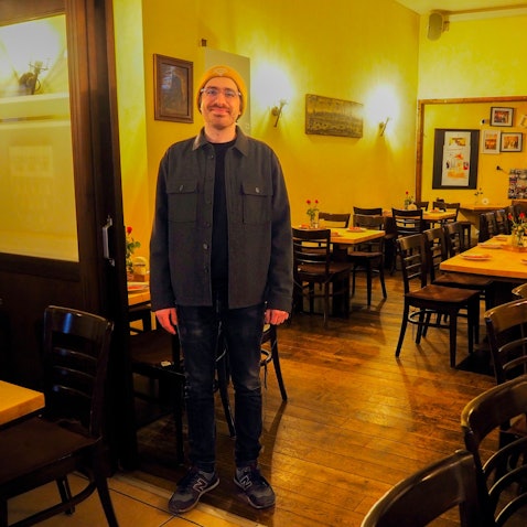 Ein Mann mit Mütze und Brille steht im Gastraum eines Brauhauses.