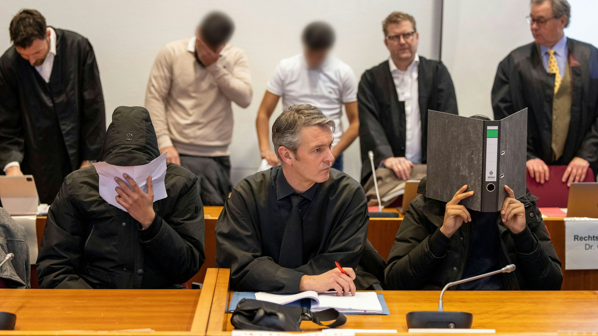 Vier der sieben Angeklagten und ihre Rechtsanwälte warten im Gerichtssaal auf den Beginn des Prozesses gegen sieben Angeklagte wegen Landfriedensbruch.