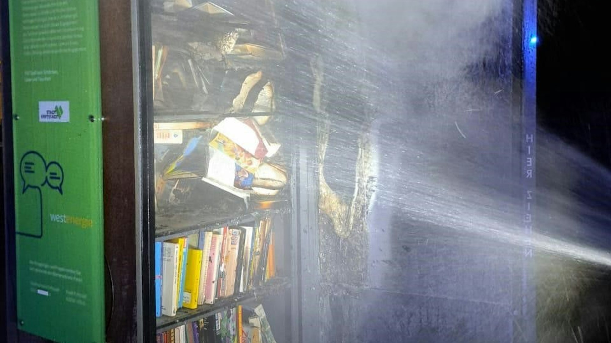 Ein brennender Bücherschrank wird mit Wasser gelöscht.