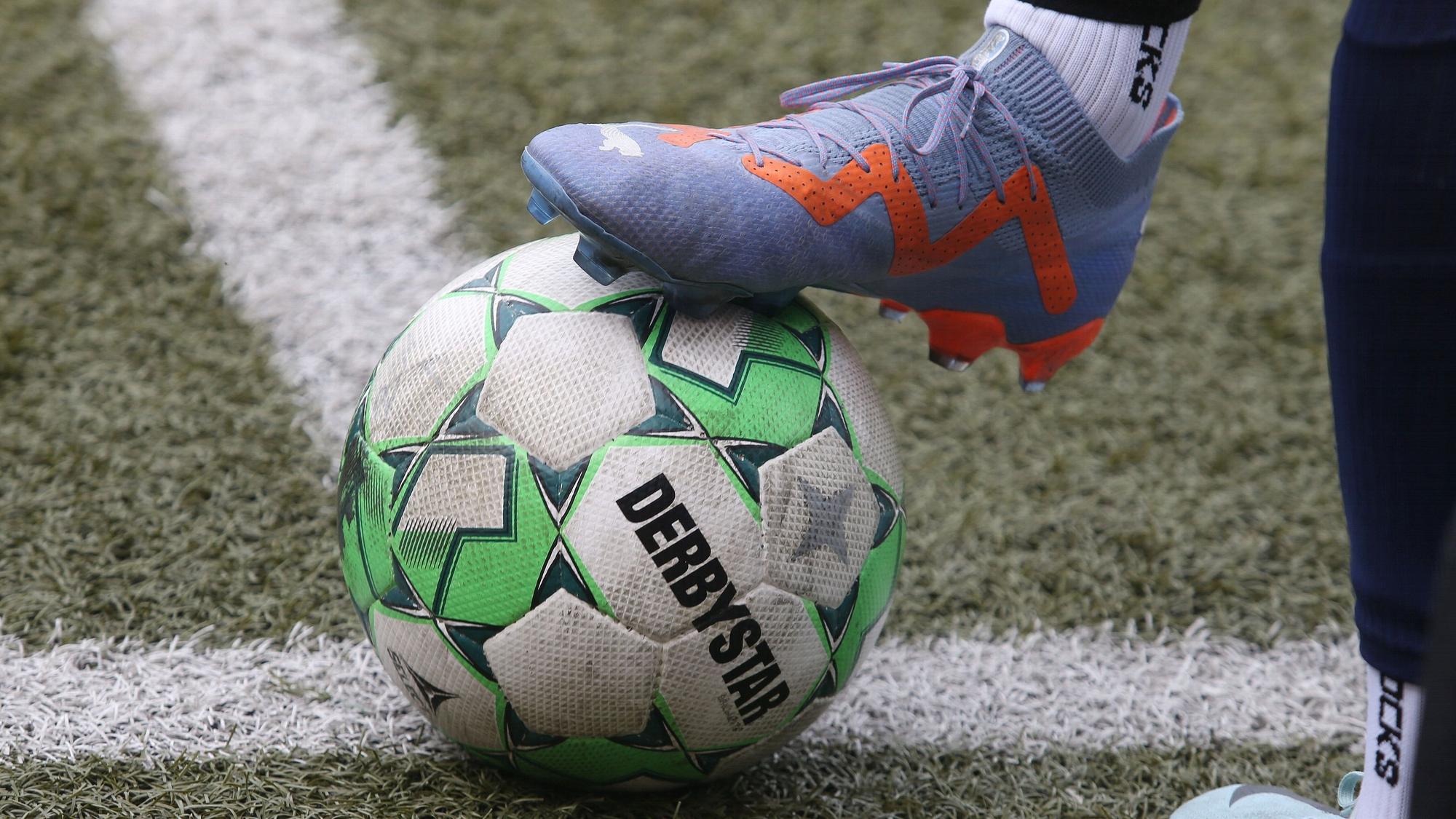 Auf der Linie liegt ein Fußball, der von einem Fuß mit Fußballschuh gehalten wird.