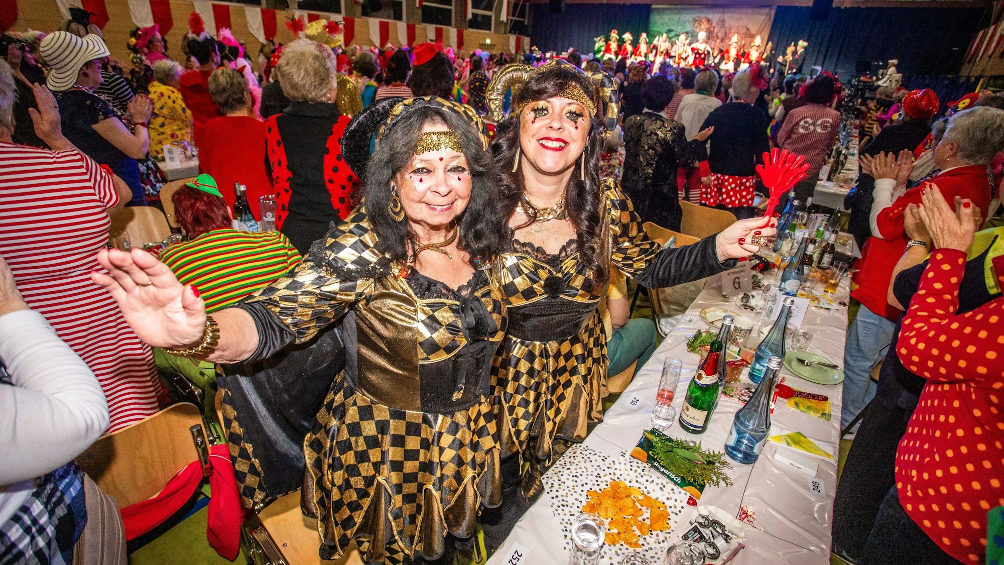 Zwei Frauen in Harlekin-Kostümen schunkeln.