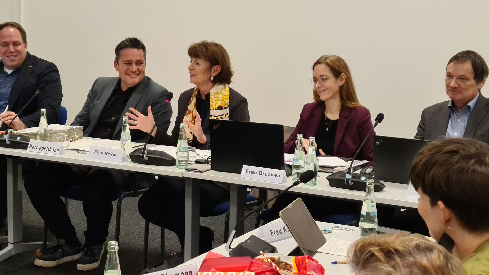 Drei Männer und zwei Frauen sitzen nebeneinander an einem Konferenztisch.