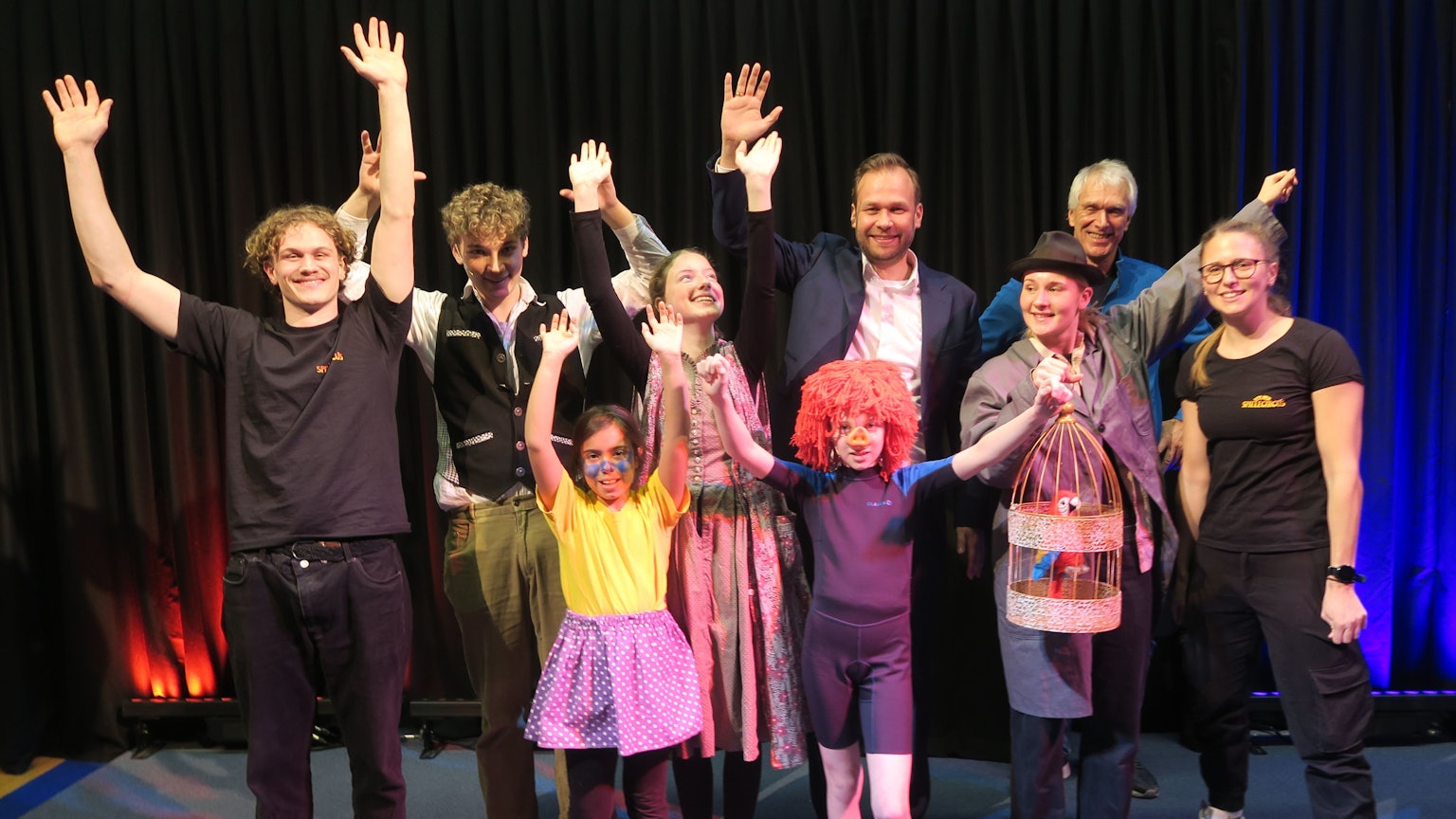 Die Hauptdarsteller und Mitglieder des Kölner Spielecircus'-Teams mit Dezernent Robert Voigtsberger und Geschäftsführer Heiner Kötter stehen auf der Bühne und strecken die Hände in die Höhe.
