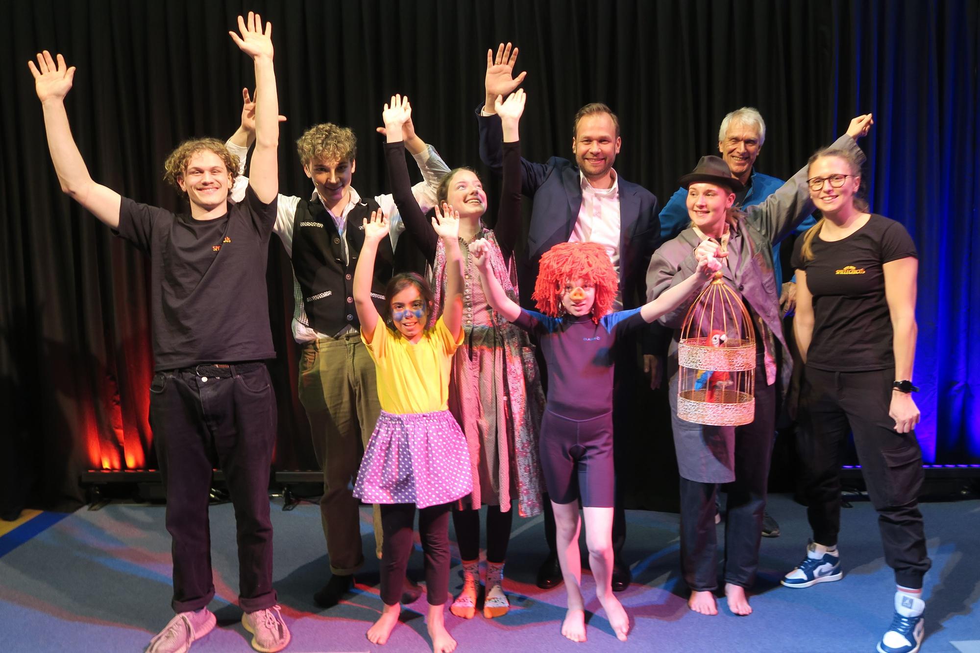 Die Hauptdarsteller und Mitglieder des Kölner Spielecircus'-Teams mit Dezernent Robert Voigtsberger und Geschäftsführer Heiner Kötter stehen auf der Bühne und strecken die Hände in die Höhe.