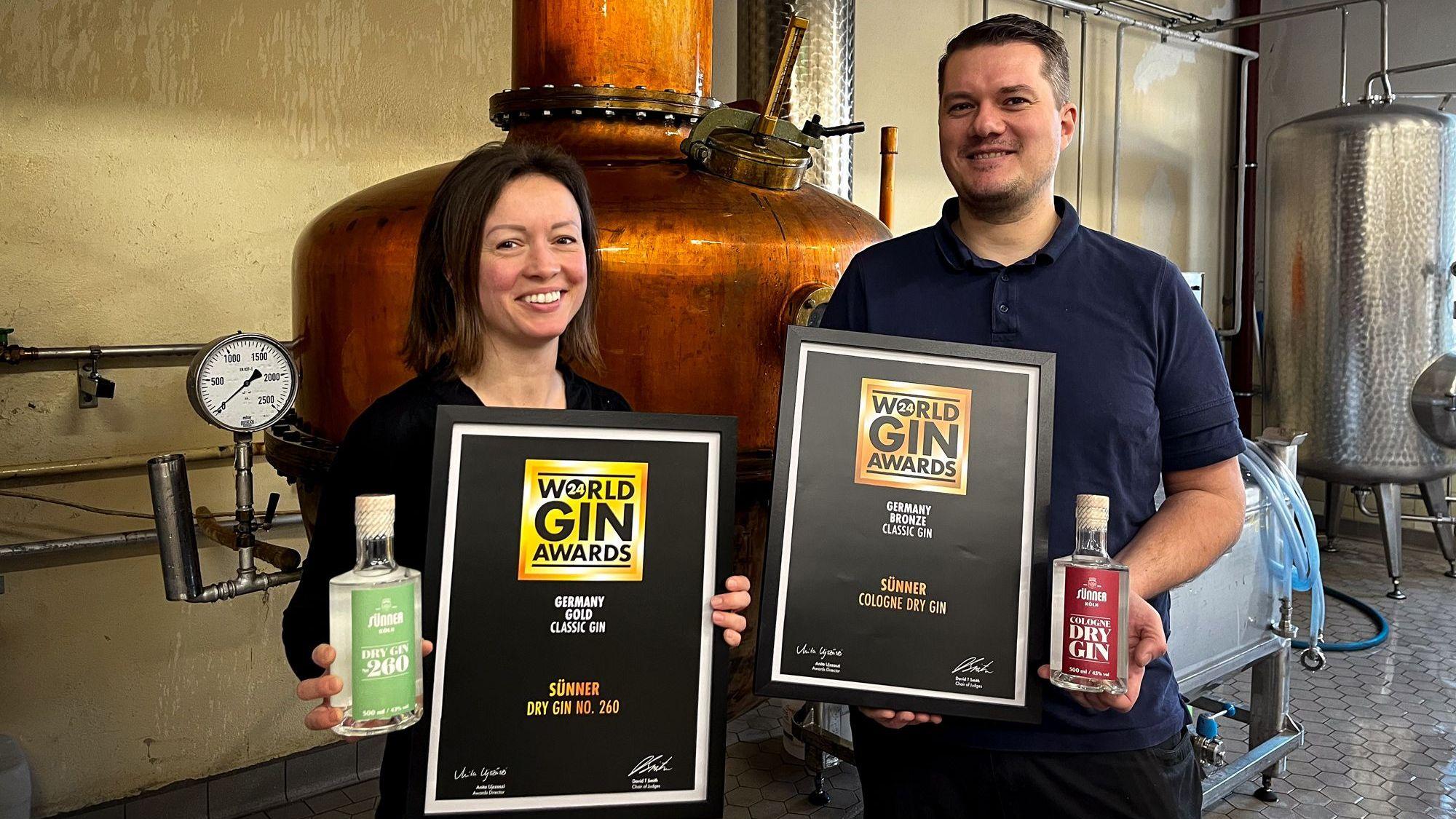 Samantha und Martin Sittkus, Destillateurin und Braumeister bei Sünner, halten jeweils eine Flasche Gin ihrer Hand.