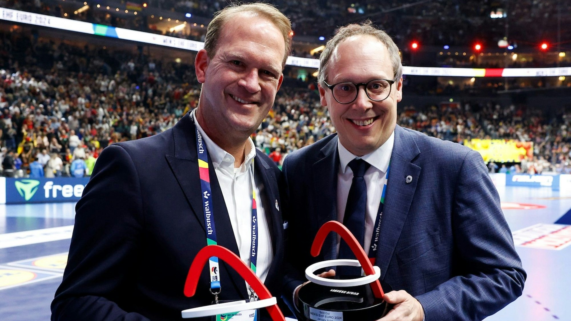 Zwei Männer in blauen Sakkos, weißen Hemden und mit einem Award in der Hand